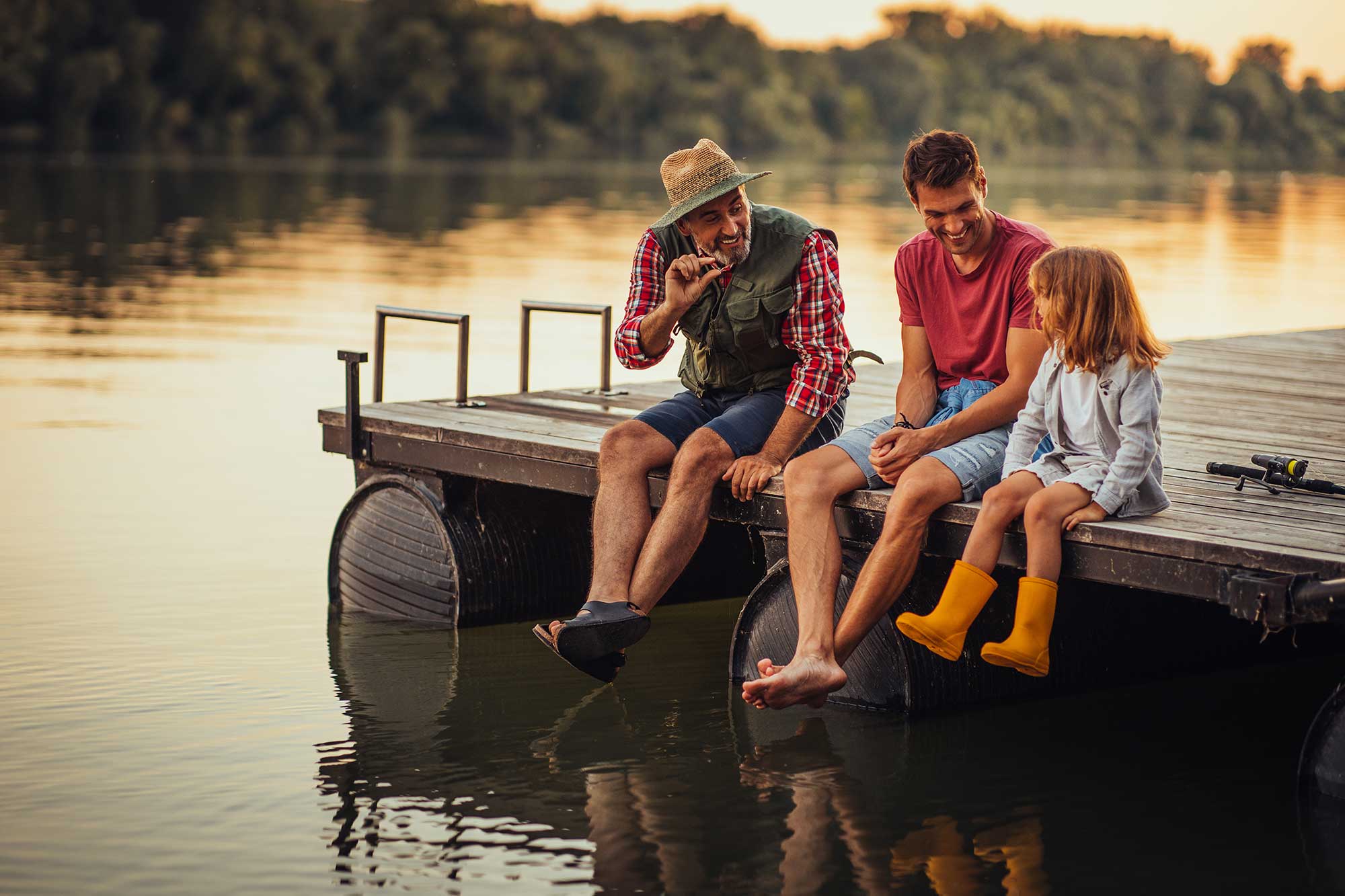 Grandfather, father, and daughter telling fishing stories on a lake dock